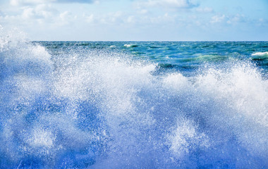 White sea spray of a wave breaking on the beach with a rough sea and sky behind