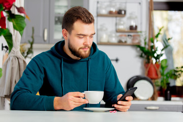 young man drinks coffee and uses a mobile phone