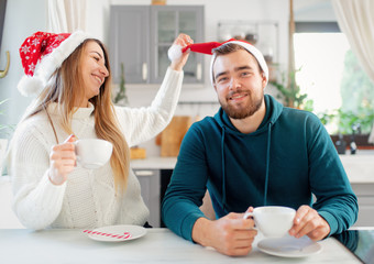 young married couple in Christmas hats drinks coffee in the kitchen