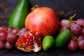 Red pomegranate, avocado, feijoa (acca) and bunches of grapes on dark background. Fruit and berries background. Healthy food.