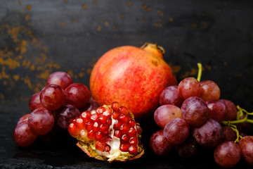 Red pomegranate and bunches of grapes on dark background. Still life fruit background.