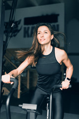 Fototapeta na wymiar Purposeful young slim fit girl with flying hair on a stationary bike in the gym intensively burns calories - a tough sport with heavy loads