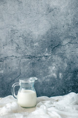 Glass carafe of fresh milk on a wooden white table with white fabric
