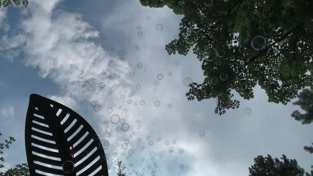 Soap bubbles flying on blue sky with clouds, floating in the air