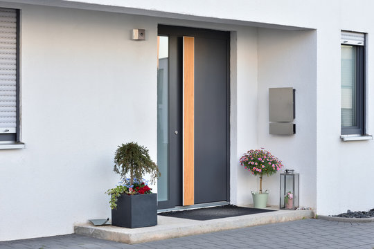 A large gray pot with a green bush in front of the entrance to the house next to the front gray door.