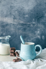 Obraz na płótnie Canvas Blue pastel coffee mug, bottle of milk and chocolate on a rustic white table and fabric