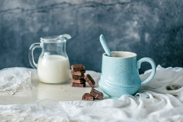 Obraz na płótnie Canvas Blue pastel coffee mug, bottle of milk and chocolate on a rustic white table and fabric