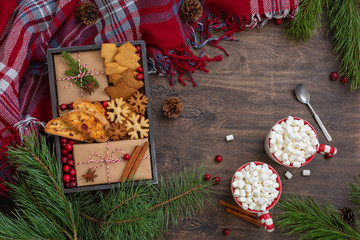 Homemade christmas cookies and wrapped presents with fresh cranberries in a wooden box with two mugs with marshmallows