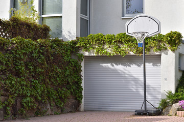 A basketball hoop installed next to a garage in a private house. Garage, overgrown with climbing...