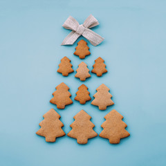Christmas tree made of homemade shortbread cookies on light blue background with cute cotton ribbon on top. Flat lay style, minimal composition. Festive pastry. New Year postcard.