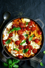 Pasta casserole with tomatoes and mozzarella cheese in a cast iron pan. Top view with copy space.