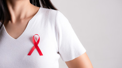 Closeup of red badge ribbon on woman chest to support AIDS Day. Healthcare, medicine and AIDS...