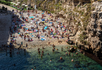 Polignano a Mare, Italy - September 17, 2019: People relax and swimming on lovely beach Lama Monachile in Polignano a Mare, Adriatic Sea, Apulia, Bari province, Italy,