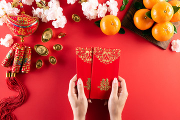 Chinese new year festival decorations. Woman hand holding pow or red packet, orange and gold ingots on a red background. Chinese characters FU means fortune good luck, wealth, money flow.