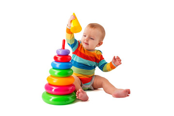 Fototapeta na wymiar Charming cute baby in overalls plays with a colored plastic pyramid sitting on a white background. A child collects a colored pyramid