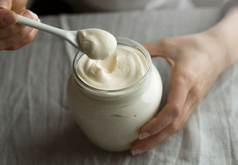 Woman holds in her hands a glass jar of mayonnaise or sour cream with a spoon. - 305555284