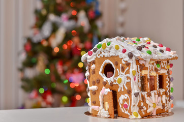 Homemade gingerbread house on the background of Christmas tree and lights.