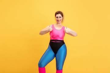 Fototapeta na wymiar Young caucasian plus size female model's training on yellow background. Copyspace. Concept of sport, healthy lifestyle, body positive, fashion, style. Stylish woman smiling with thumbs up.