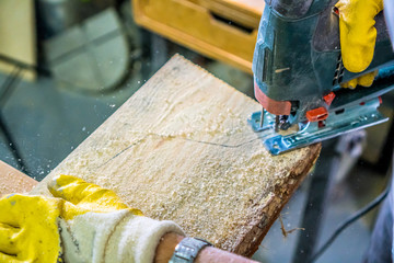Carpentry background. Carpenter hands with fretsaw. Carpenter use electric fretsaw to cut the desk. .