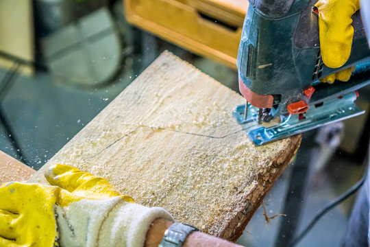 Carpentry background. Carpenter hands with fretsaw. Carpenter use electric fretsaw to cut the desk. .