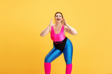 Fototapeta na wymiar Young caucasian plus size female model's training on yellow background. Copyspace. Concept of sport, healthy lifestyle, body positive, fashion, style. Stylish woman calling with hands covering mouth.