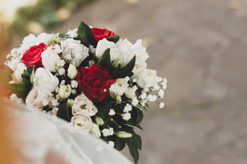 soft focus of bridal hands holding fresh bouquet with roses and leaves with white ribbon in front of green grass
