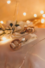 selective focus of golden wedding rings on white decorative cushion in front of blurred shiny lights