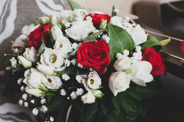 close up of bridal bouqet with red, white roses and green leaves at home