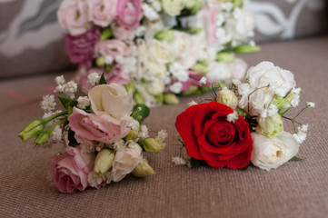 soft focus of boutonnieres with pink, red and white flowers in front of bridal bouquet with roses on couch at home