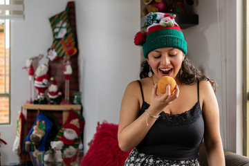 Colombian woman at Christmas with Christmas hat eating buñuelo typical Colombian food