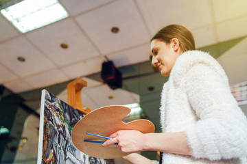 Young beautiful female girl woman artist painter painting standing in front of the canvas easel at home or studio paint holding easel and brush
