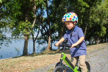 Obraz premium Cute little Asian 3 - 4 years old toddler boy child wearing safety helmet learning to ride first balance bike in sunny summer day, kid playing & cycling at park, Cycling with young kids concept 