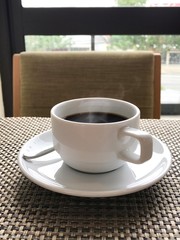 The white ceramic cup of hot coffee is on the table.