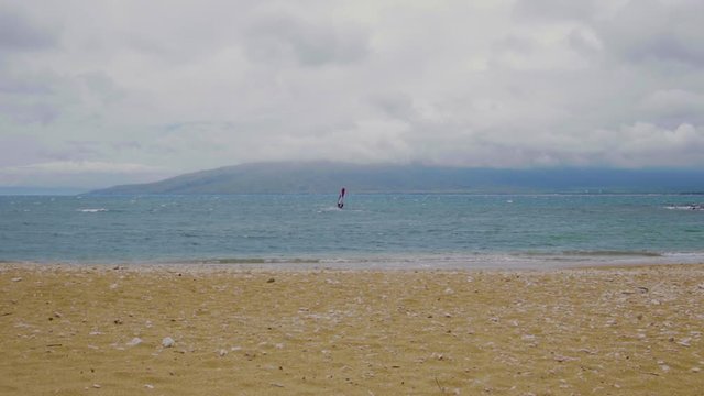 Disparo manual desde la playa a una persona que practica windsurf en la costa de Maui en un d&iacute;a nublado