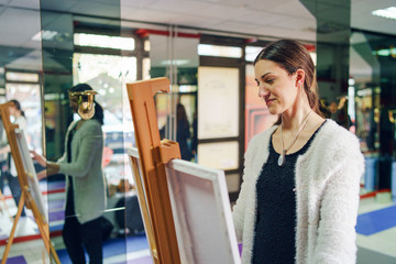 Young beautiful female girl woman artist painter painting standing in front of the canvas easel at home or studio paint