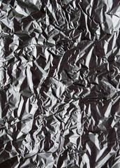Crumpled silver aluminum foil closeup background texture. Abstract metallic paper holographic effect pattern. Vertical top view