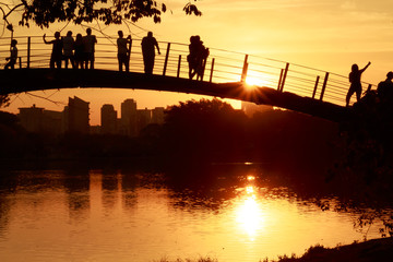 Ibirapuera Park. Awesome and colorful sunset by the lake. Beautiful sky reflections on the water. People gathered over the bridge to watch the golden hour miracle.  Sao Paulo, Brazil