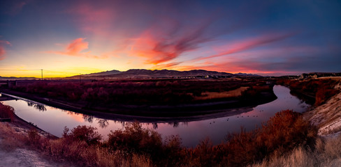Naklejka na ściany i meble Panoramic sunset over the mountains with the sky reflecting on the surface of the river