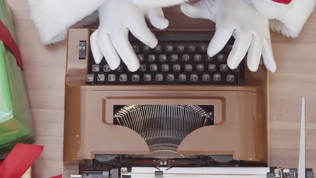 Top view of the Santa Claus writing on an old typewriter. Concept of letters, writing down an idea or names. Christmas is coming. Preparing for the Christmas night. Sales promotion. Cinematic 4K.