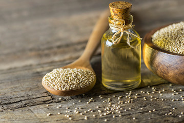 Obraz premium Glass bottle of quinoa oil with quinoa seeds in wooden spoon on wooden table. Herbs alternative medicine background concept