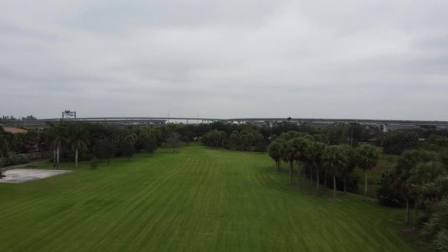 a drone shot accending in front of a field in front of some trees and a highway.