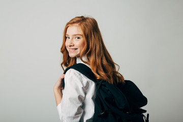 A young red-haired girl goes to school. Schoolgirl looking over her shoulder and goes to study lessons. Isolate on white background