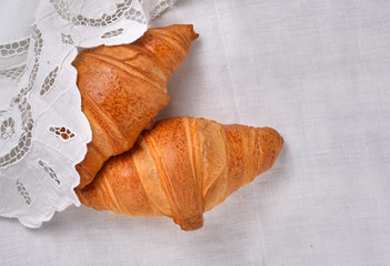 Top view on two fresh croissants on white vintage richelieu embroidery doily background with copy...