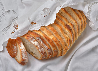 Sliced rustic bread on white linen napkin background. Home baked bread on natural vintage richelieu...