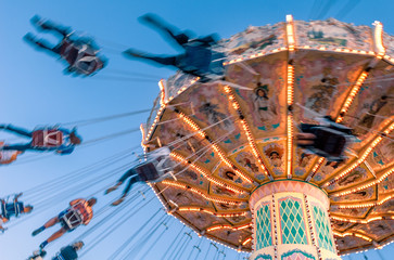 Amusement park motion blurred riders on retro vintage tilting swing against clear blue sky.
