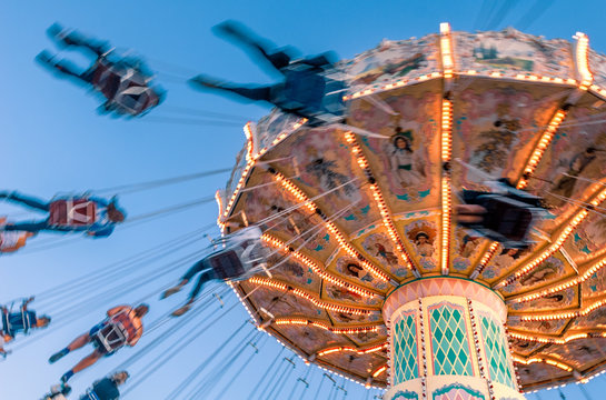 Amusement park motion blurred riders on retro vintage tilting swing against clear blue sky.