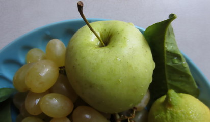  Green apple grapes lemon and leaf dewy with water on a blue plate