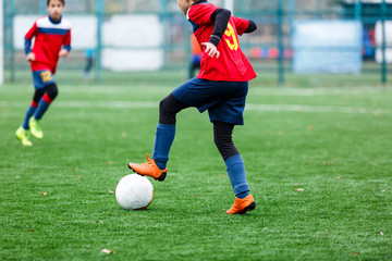 Boys in red and blue sportswear plays football on field, dribbles ball. Young soccer players with ball on green grass. Training, football, active lifestyle for kids concept 
