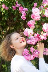 Fototapeta premium Charming girl at pastel pink rose blossom. Summer time. Beautiful young woman holding blooming rose flowers. Blossom around. Flowers of pink rose.