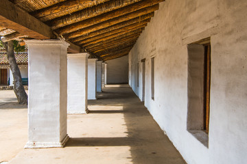 Long exterior corridor with white plastered columns and walls under a rustic wooden roof